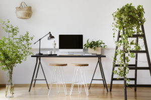 DLO office moving experts - Computer desktop on desk with lamp in white freelancer's interior with plants and stools. Real photo